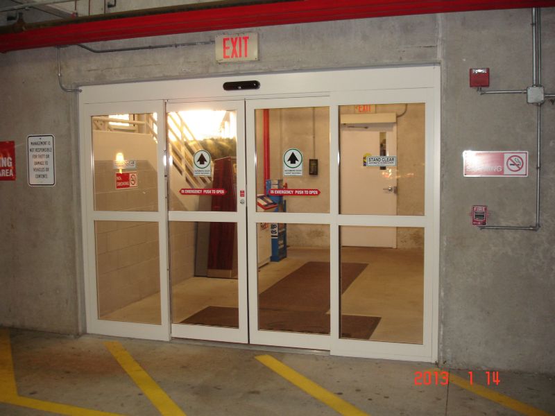 Automatic bi-parting sliding doors retroifitted into an existing wall opening in a parking garage